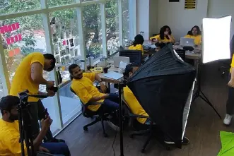 a group of people in yellow shirts in a room with light setup for a photoshoot.